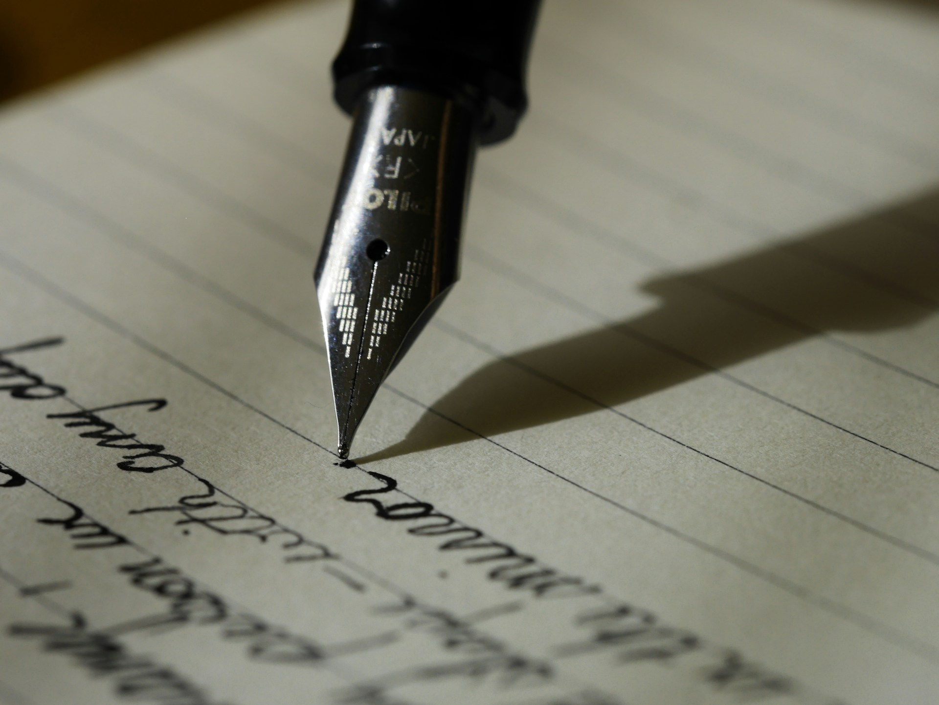 Close-up of a fountain pen writing cursive words on a lined notebook page, cover image for StudyZoneHub's step-by-step guide on how to write an essay outline with examples and templates for students.