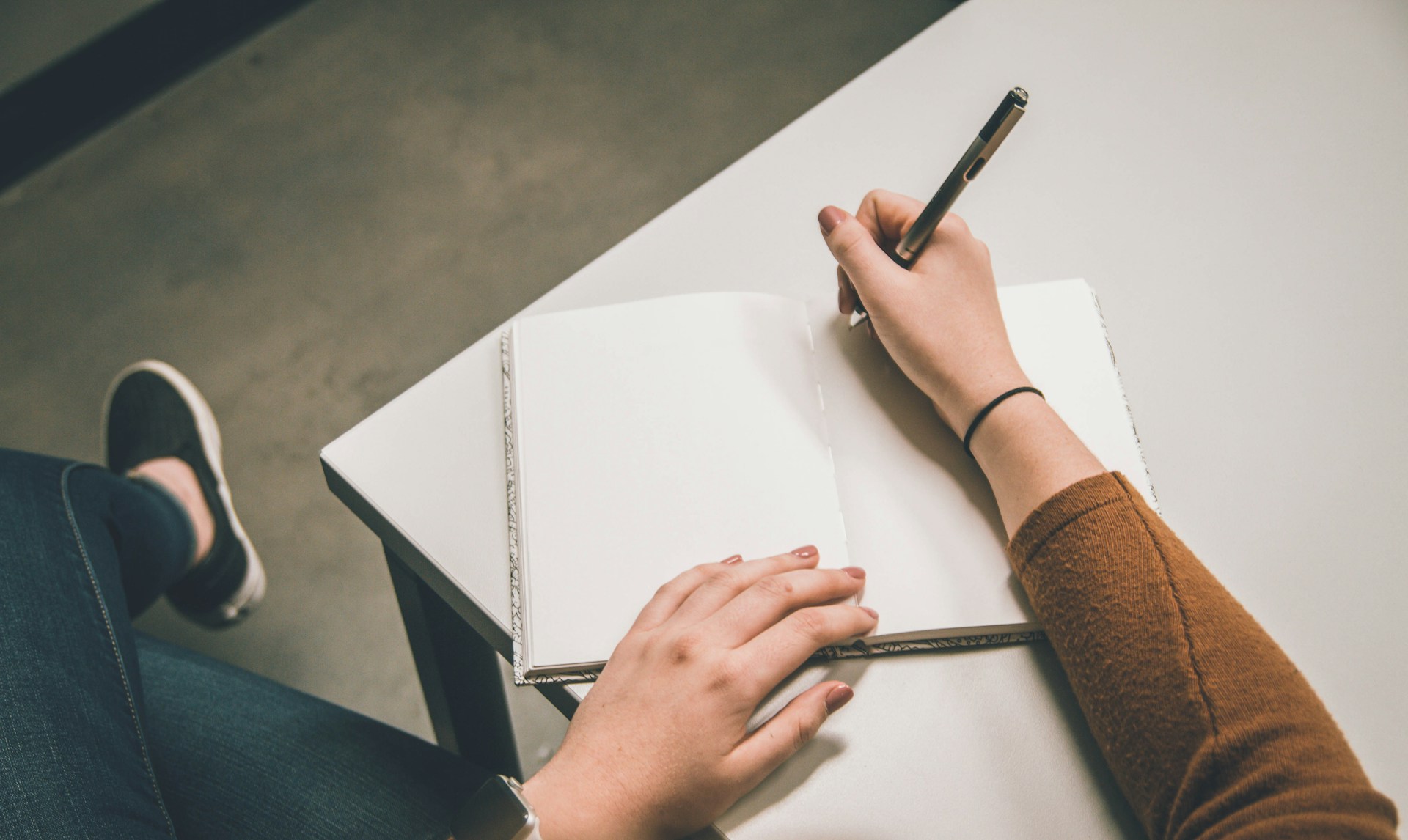 Overhead view of a student writing in an open blank notebook with a pen, illustrating the 10 best note taking methods for students to study smarter and remember more.