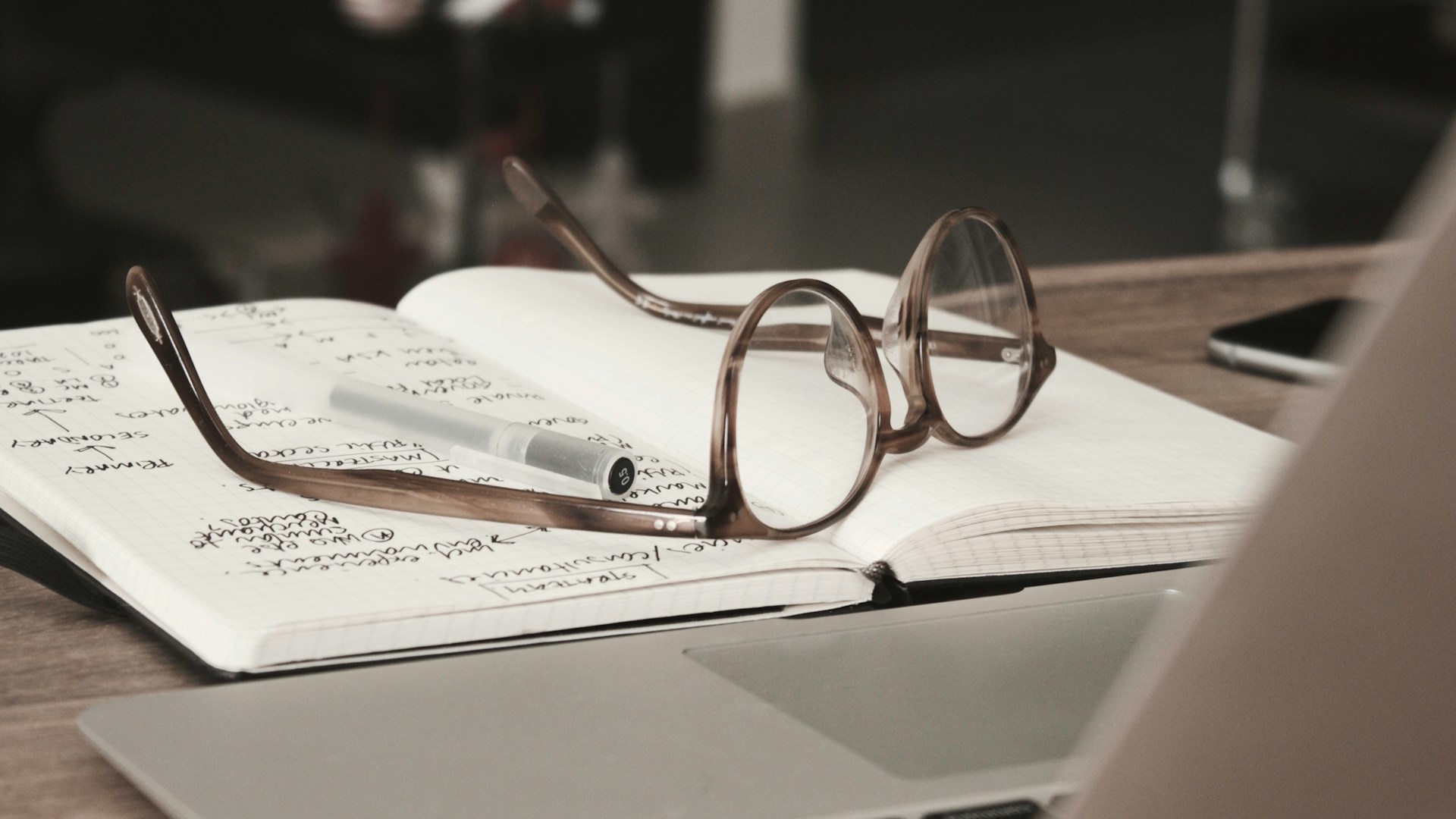 An open handwritten notebook with round glasses resting on top next to a laptop, a warm study desk scene for a guide on how to study when you have no motivation.